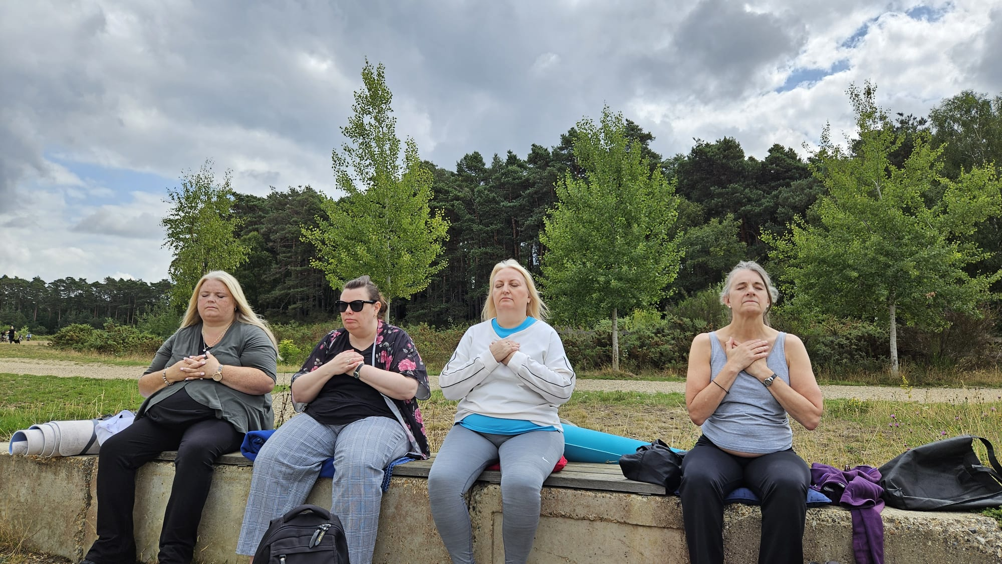 Small group of participants sitting together on a wooden platform meditating during the Berkshire Forest Retreat by Nikita Thakrar in a peaceful forest setting.