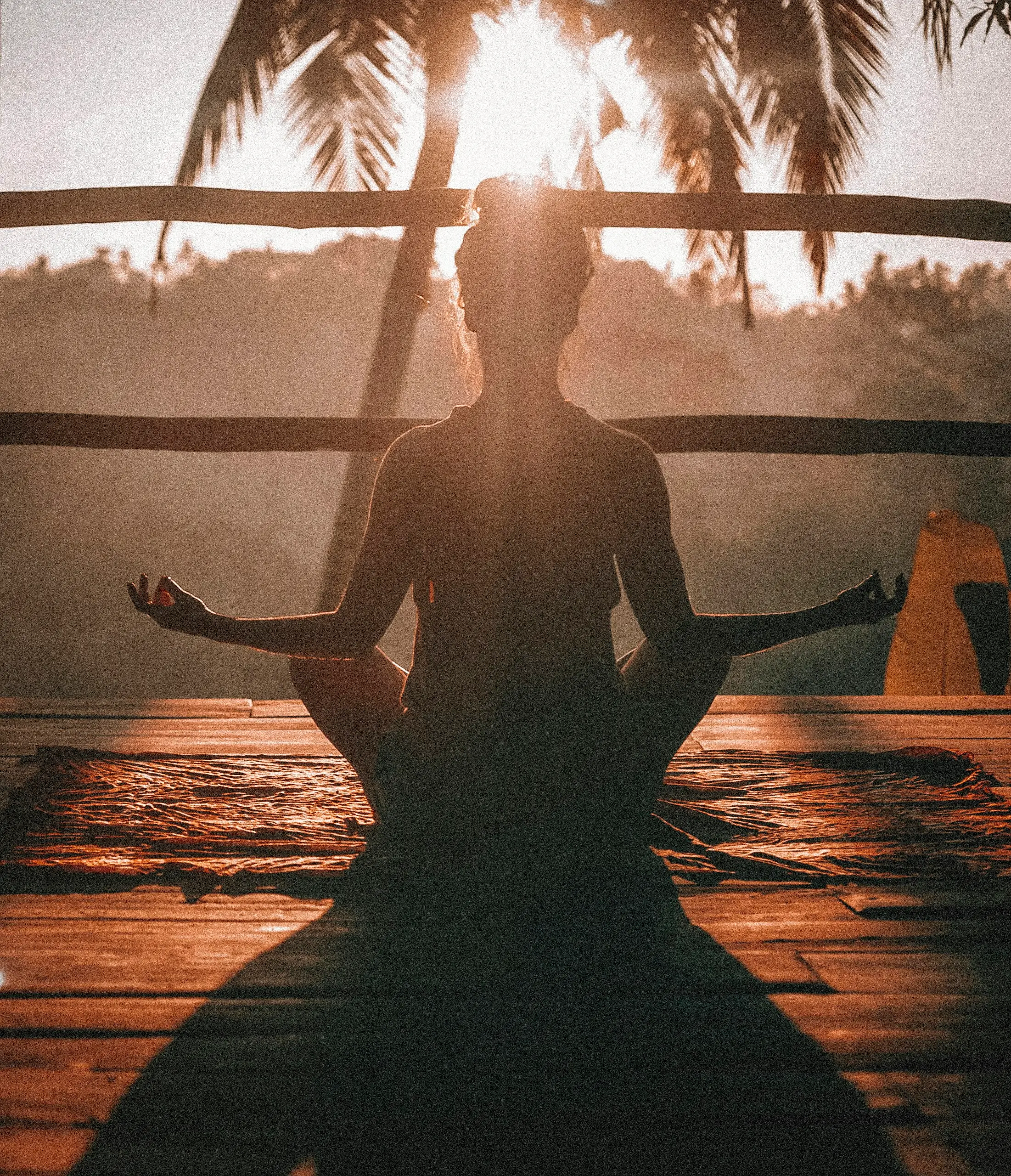 Woman meditating cross-legged at sunrise in a tropical setting, warm light glowing around her silhouette during a peaceful VIP Dharma Day with Nikita Thakrar in Berkshire.