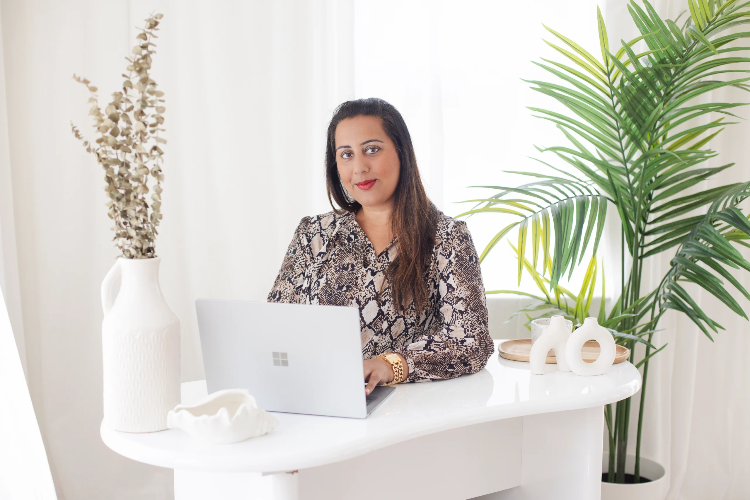 Nikita Thakrar sitting at a white desk, typing on her laptop while creating healing videos by Nikita Thakrar that share soulful teachings, emotional clarity, and grounded spiritual wisdom.