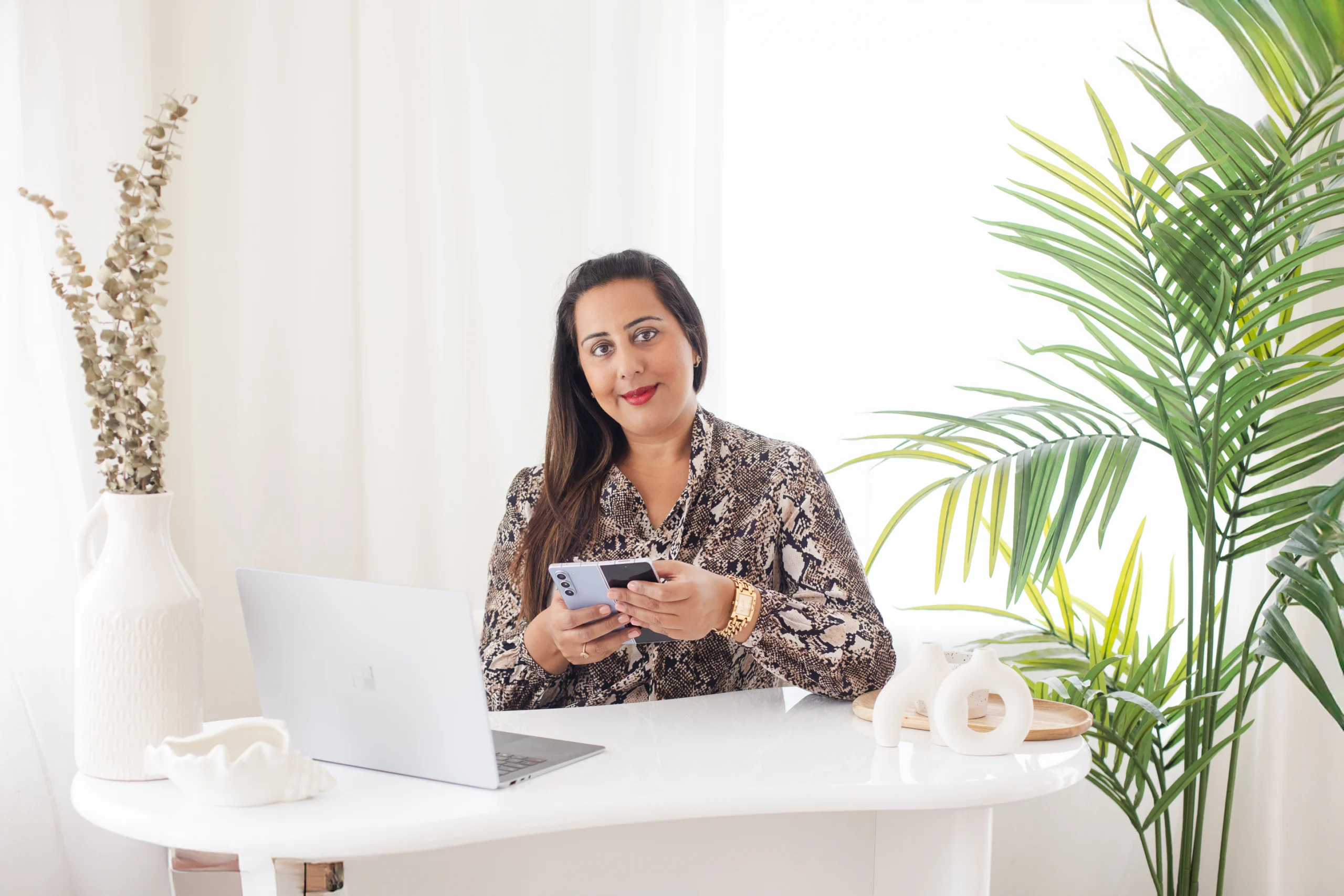 Nikita Thakrar smiling gently while seated at a desk with her laptop, preparing healing videos by Nikita Thakrar that offer compassionate guidance, personal insight, and spiritual reflection.