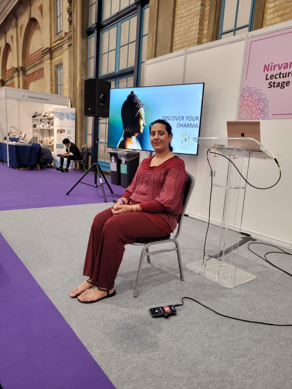 Nikita Thakrar seated on a chair at the Nirvana Lecture Stage, with a “Discover Your Dharma” presentation displayed on a screen behind her at a wellness event.
